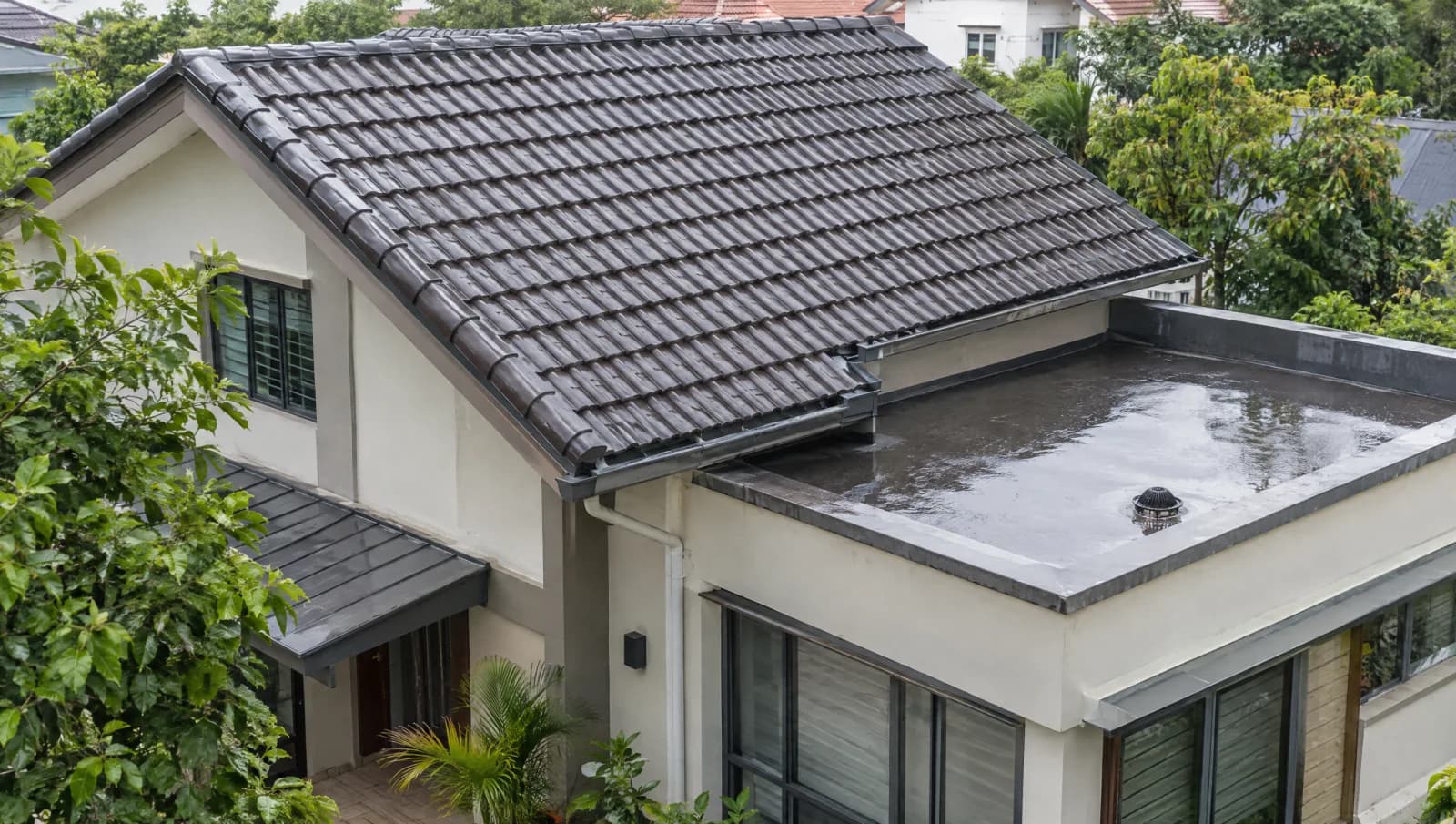 Pitched tiled main roof beside a flat-roof extension on a Singapore landed house after rain.