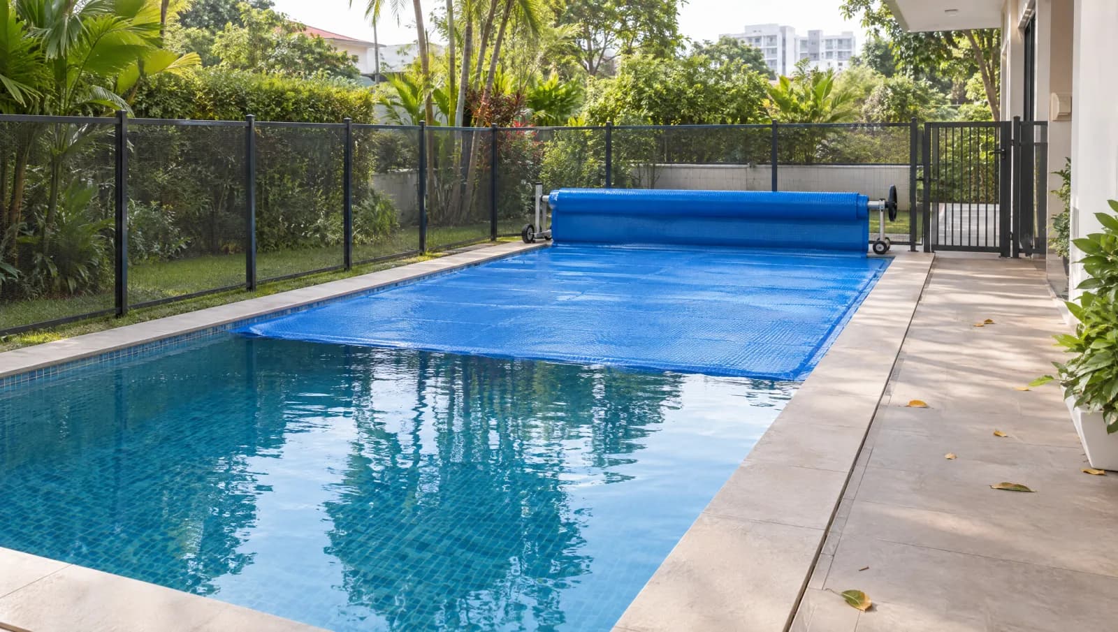 Thermal pool blanket rolled onto a reel inside a separately fenced pool area.