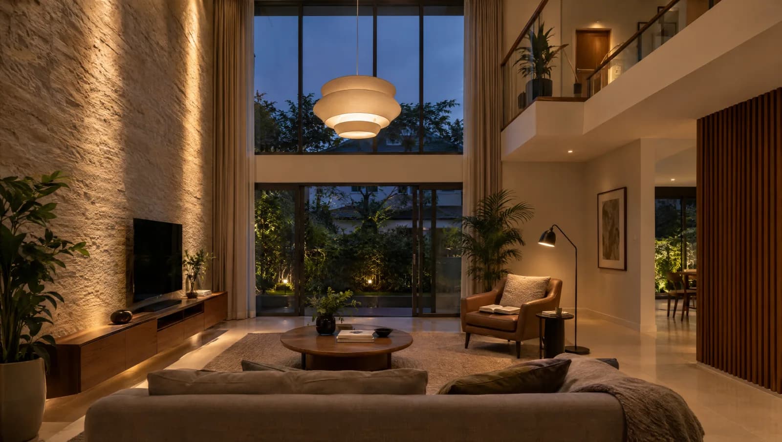 Double-height living room with a pendant, illuminated wall and local reading light at dusk.